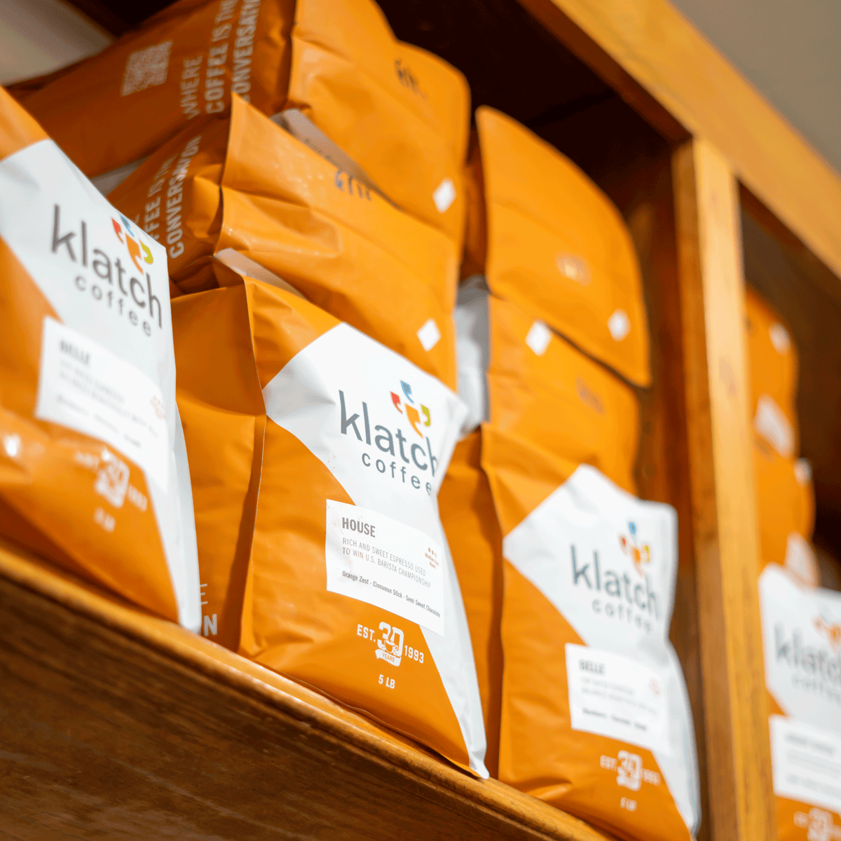 Klatch Coffee 5 lb wholesale coffee bags displayed on wooden shelves, featuring the signature orange and white packaging.