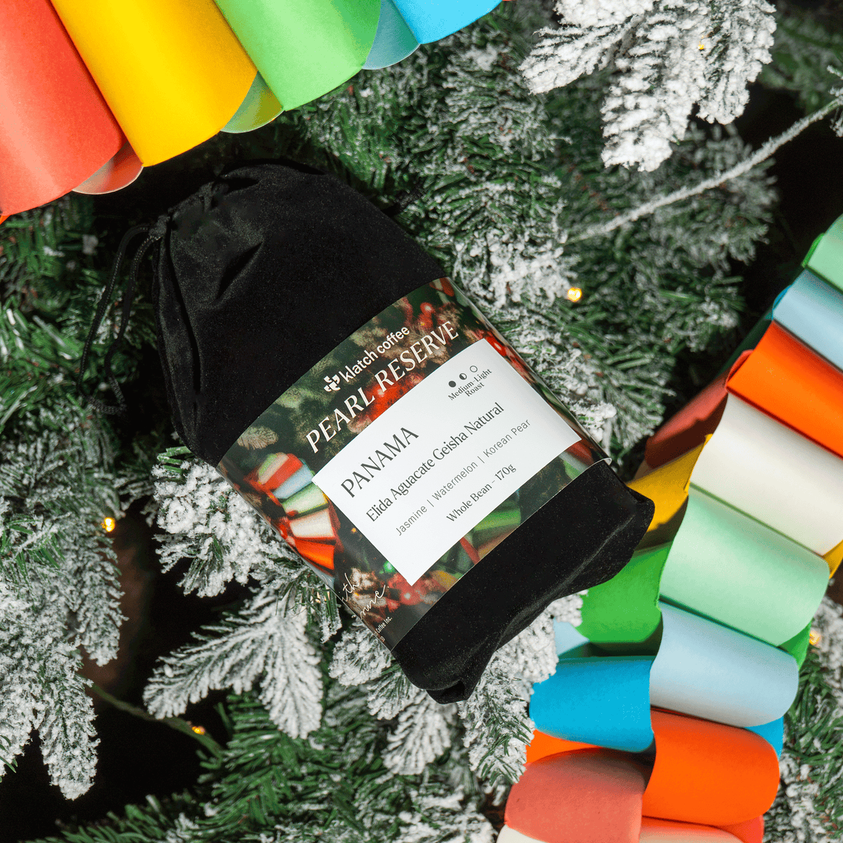 A black drawstring velvet pouch containing a rolled gold leaf specimen labeled 'PEARL RESERVE PANAMA', placed among green frosted pine branches and colorful rolled paper garlands.