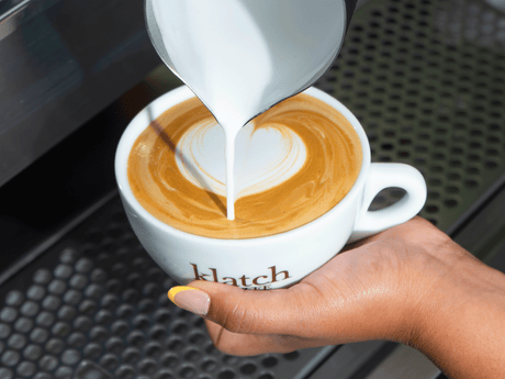 Hands pouring latte art into a mug.