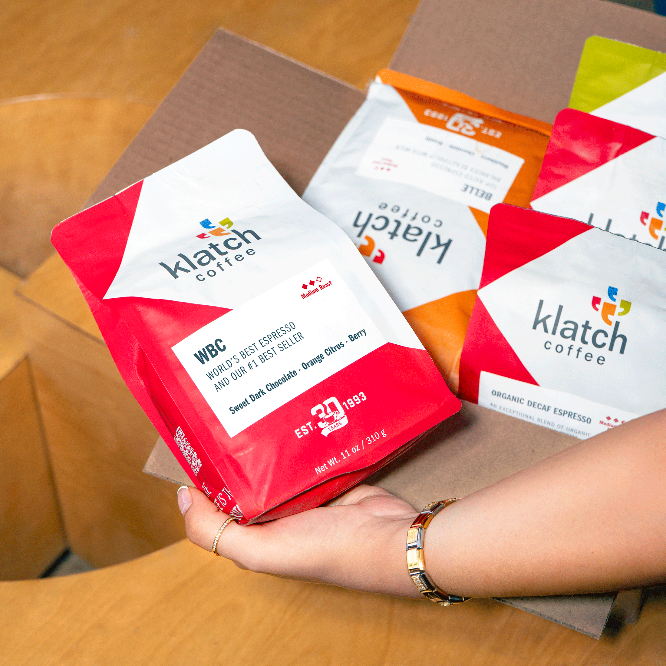 Hand holding a bag of WBC Espresso above a shipping box filled with coffee bags.