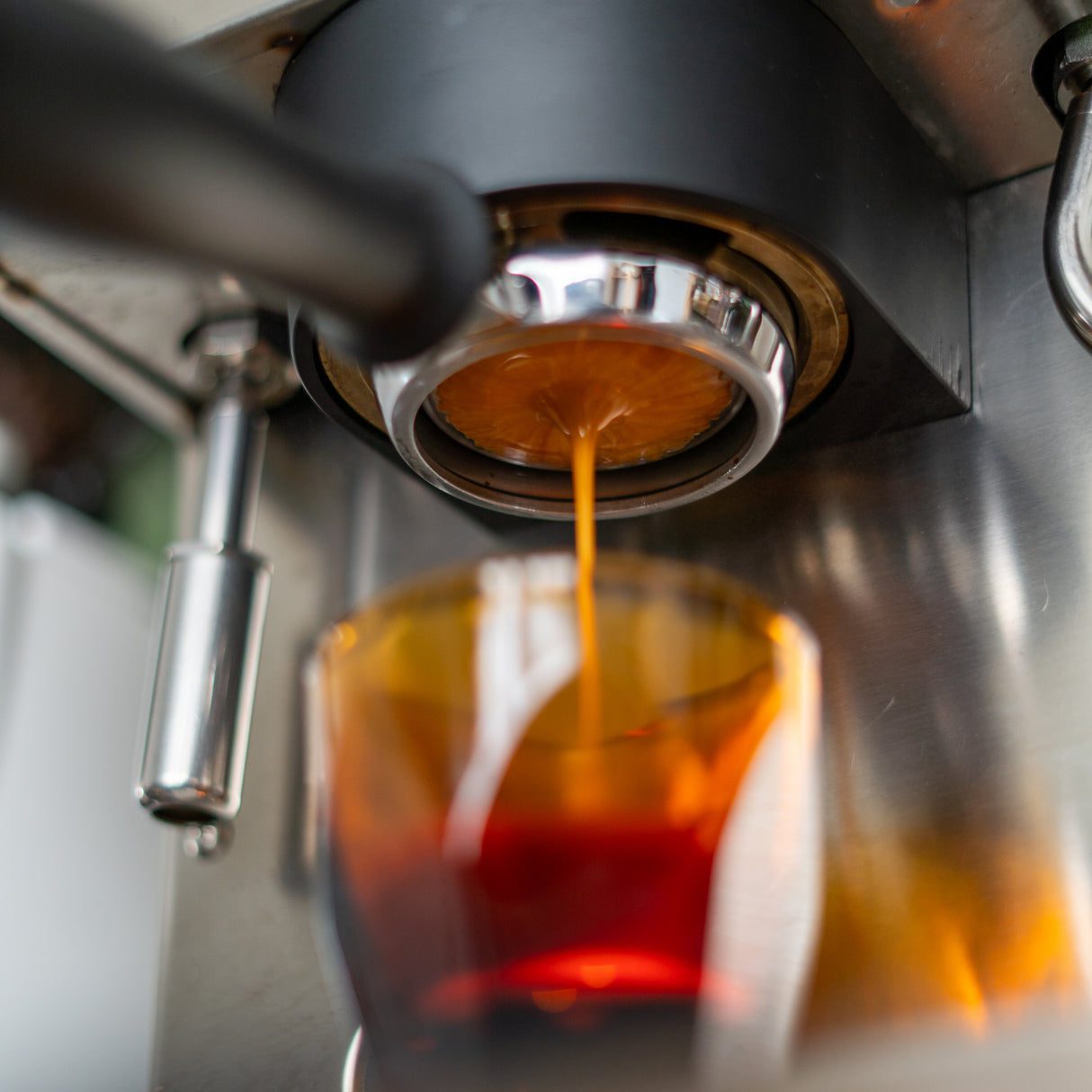 Espresso shot pouring into orange cup