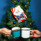 Klatch Original Christmas coffee bag in a Christmas tree with two hands cheering mugs in front of a blue background.