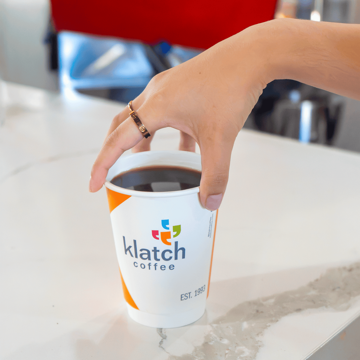 Hand reaching for an orange Klatch Coffee cup on a countertop.