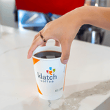Hand reaching for an orange Klatch Coffee cup on a countertop.