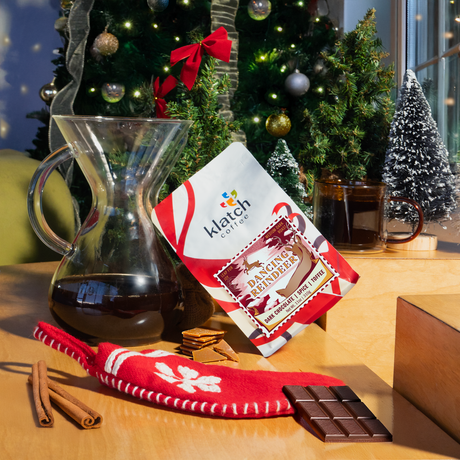Dancing Reindeer coffee bag leaning against a Chemex with a Christmas tree and coffee mug in the background.