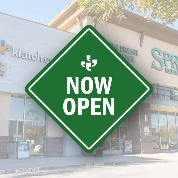 A green diamond-shaped vector sign with the Klatch Coffee logo at the top and “Now Open” beneath it, placed over a photo of Sprouts and a Klatch sign.