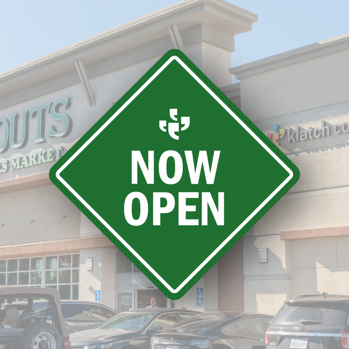 A green diamond-shaped vector sign with the Klatch Coffee logo at the top and “Now Open” beneath it, placed over a photo of Sprouts and a Klatch sign.