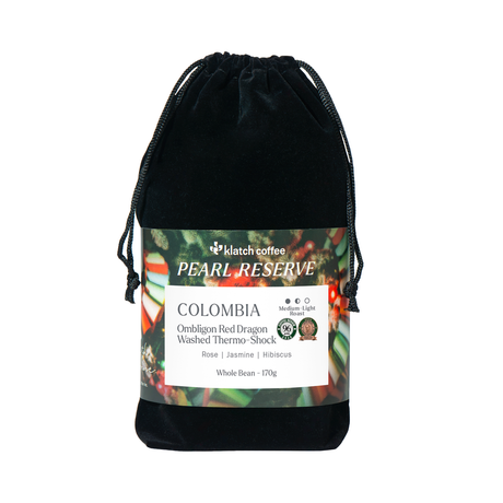 A black velvet drawstring pouch containing Klatch Coffee Pearl Reserve Colombia whole bean coffee, with a detailed product label wrapped around the middle, set against a plain white background.
