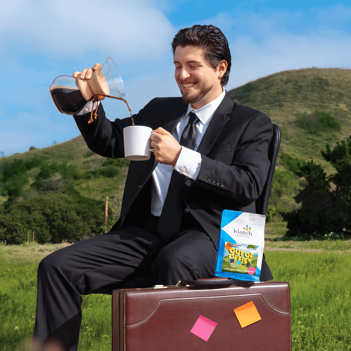 Man in a suit pouring coffee into a cup with a scenic background, a bag of Out of Office on a brief case.