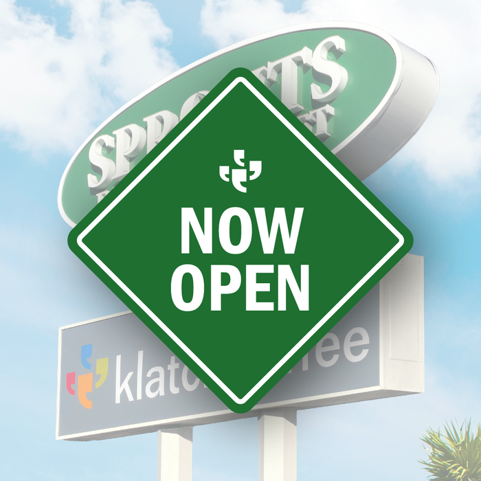 A green diamond-shaped vector sign with the Klatch Coffee logo at the top and “Now Open” beneath it, placed over a photo of Sprouts and a Klatch sign.