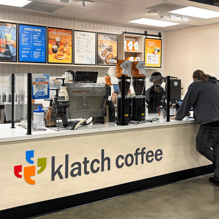 Interior of a Sprouts Farmers Market featuring a Klatch Coffee counter; a man stands at the counter, with a large Klatch Coffee logo in the foreground and menus displayed on the wall.