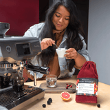 Woman making coffee using a Breville espresso machine with a bag of Pearl Reserve Kenya coffee on a wooden table.