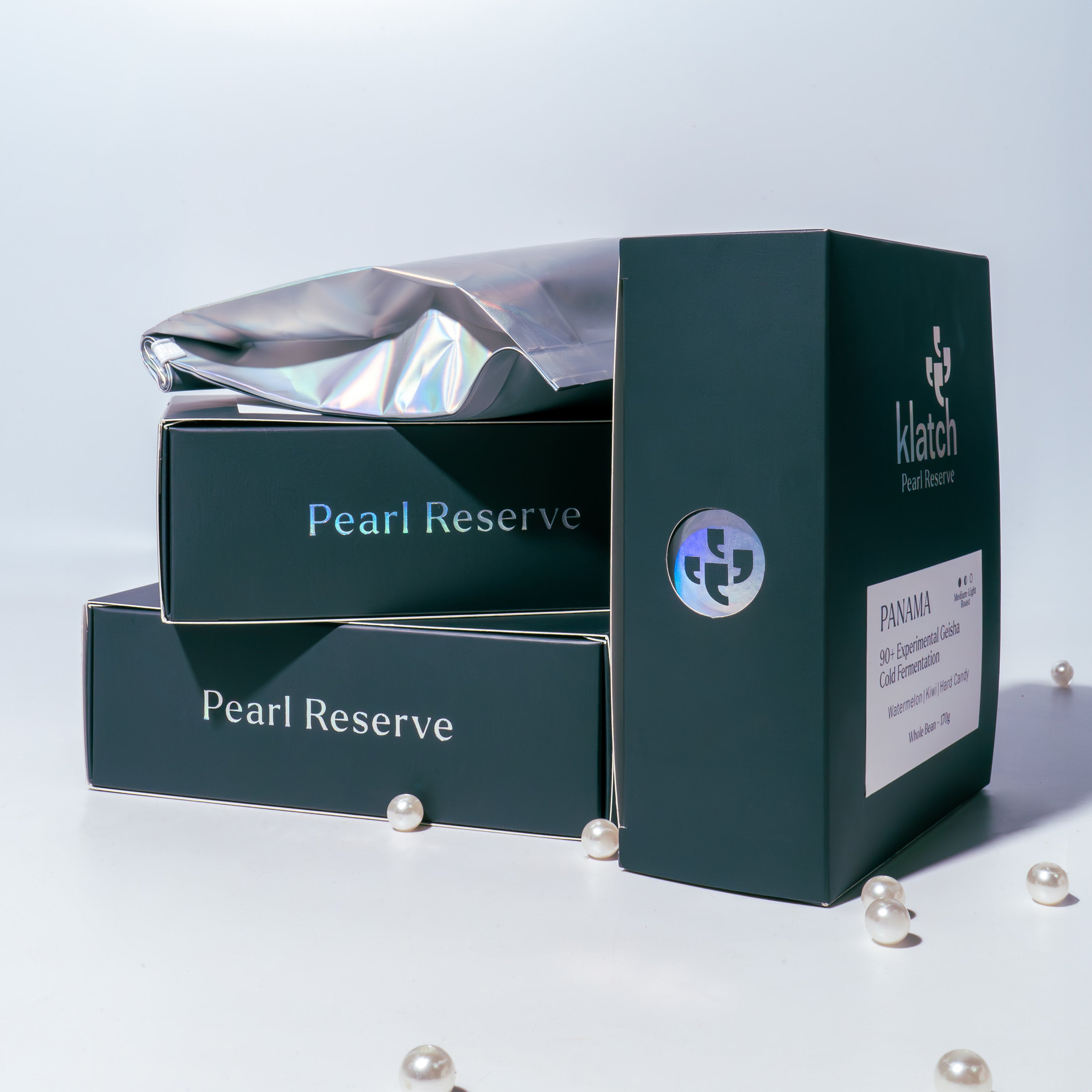 Three Klatch Pearl Reserve boxes arranged in different positions with a colorful bag, set on a white background with scattered pearls.