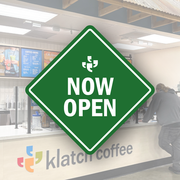 A green diamond-shaped vector sign with the Klatch Coffee logo at the top and “Now Open” beneath it, placed over a photo of a Klatch Coffee cafe. 