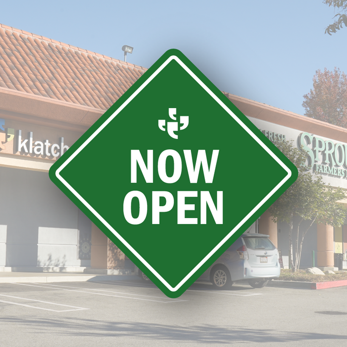 A green diamond-shaped vector sign with the Klatch Coffee logo at the top and “Now Open” beneath it, placed over a photo of Sprouts and a Klatch sign.