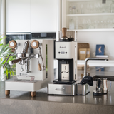 A white LELIT MaraX3 Espresso Machine set with a matching William Coffee Grinder and accessories, arranged on a kitchen countertop in a bright, modern kitchen.