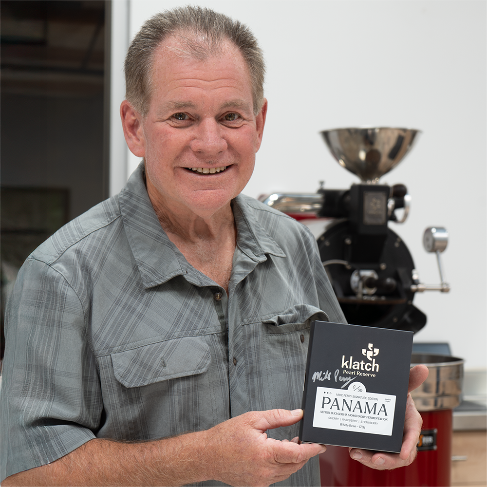 Mike holding Signed Pearl Reserve Luci box in front of a coffee sample roaster.