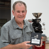 Mike holding Signed Pearl Reserve Luci box in front of a coffee sample roaster.