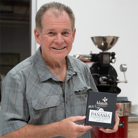 Mike holding Signed Pearl Reserve Luci box in front of a coffee sample roaster.