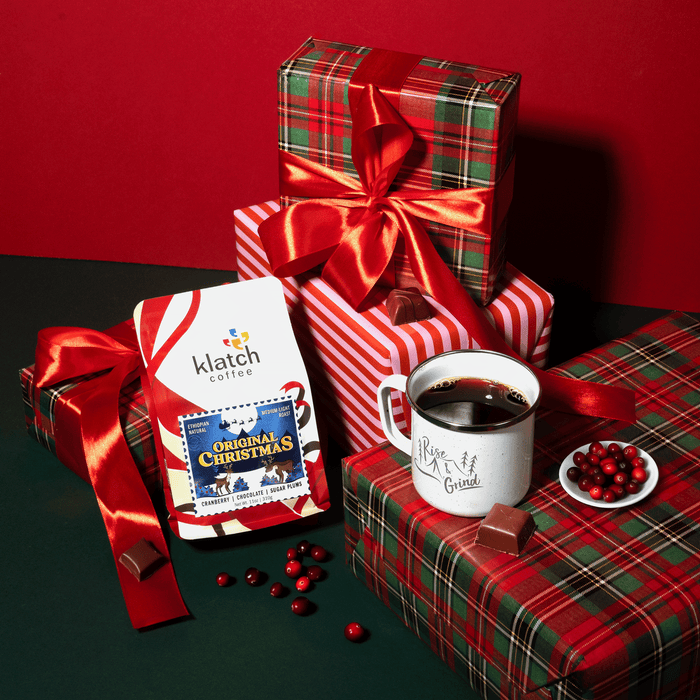 Holiday-themed gift setup with Original Christmas coffee, chocolates, and plaid wrapping paper on a red background.