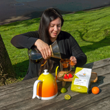 Women pouring coffee with bag of Pacamara Anaerobic Natural on picnic table with strawberries, lime, and orange.