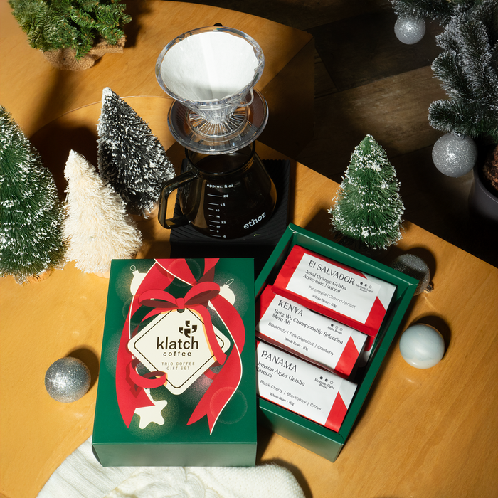 Klatch Coffee Pearl Trio box on a table beside a coffee brewer, with Christmas trees and ornaments scattered around for a festive holiday setting.