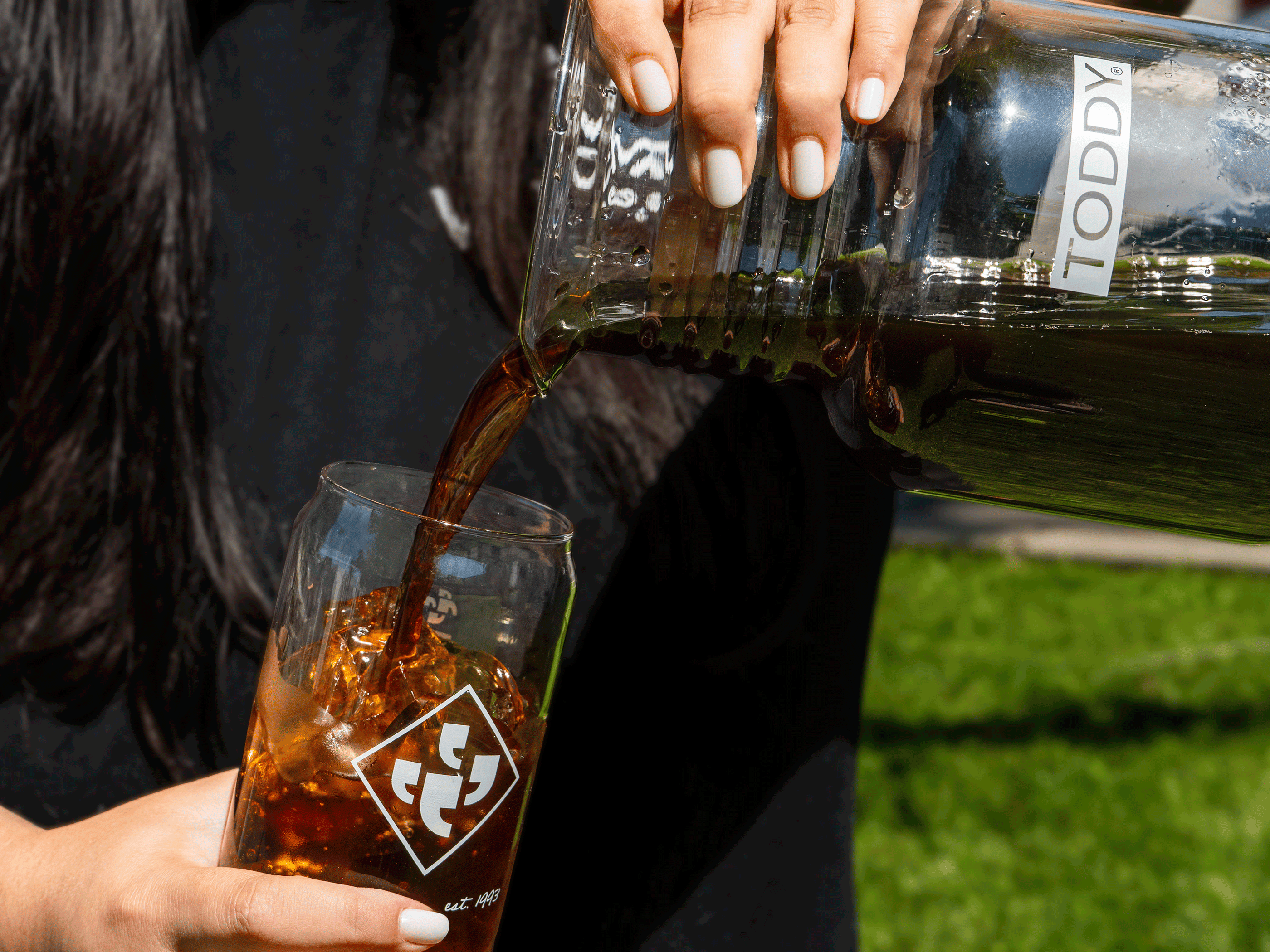 Person pouring cold brew from a Toddy brewer into a glass featuring the Klatch Coffee logo.