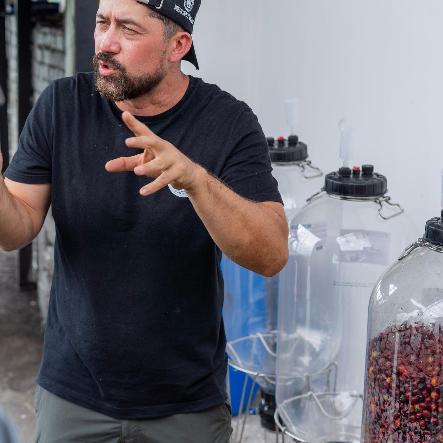 Edwin Norena speaking about the Carbonic Maceration process with clear barrels with coffee cherries next to him.