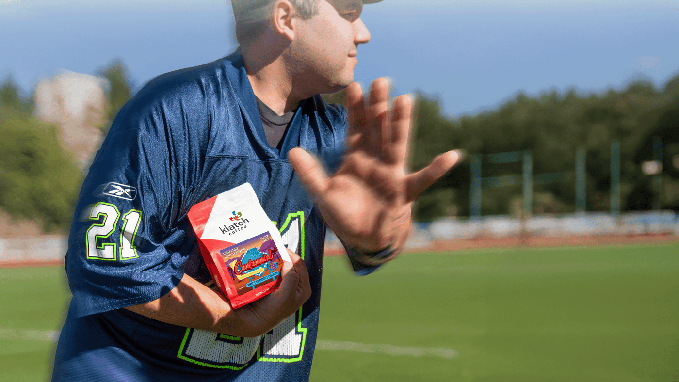 Person in sports jersey holding a a bag of Centennial on a football field.