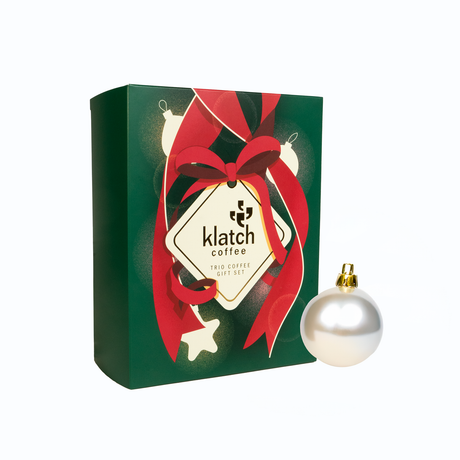 Holiday Gift box with a red ribbon and 'Klatch Coffee' label with decorative a pearl ornament on a white background.