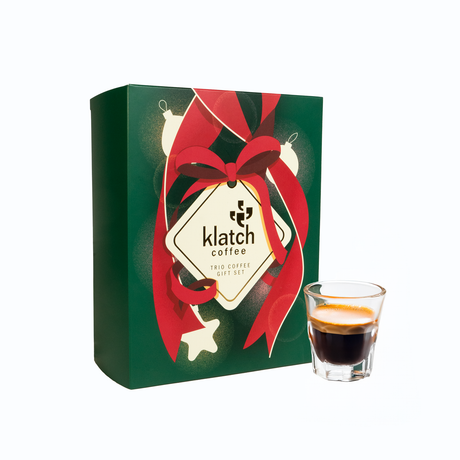 Holiday Gift Box with red ribbon and 'Klatch Coffee' branding, next to a glass of espresso.