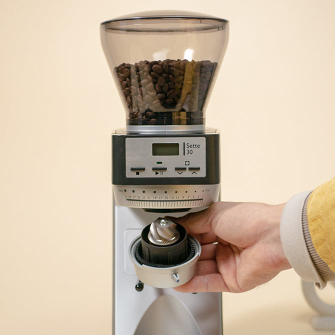 Hand adjusting the burr on a Baratza Sette 30 coffee grinder filled with coffee beans.