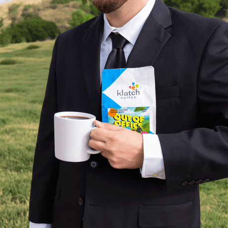 Man in a suit holding a Klatch coffee Out of Office bag of coffee and a mug outdoors.