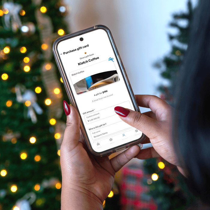 In a close-up view, a person holds a smartphone with the Klatch Coffee app open to the gift card page.