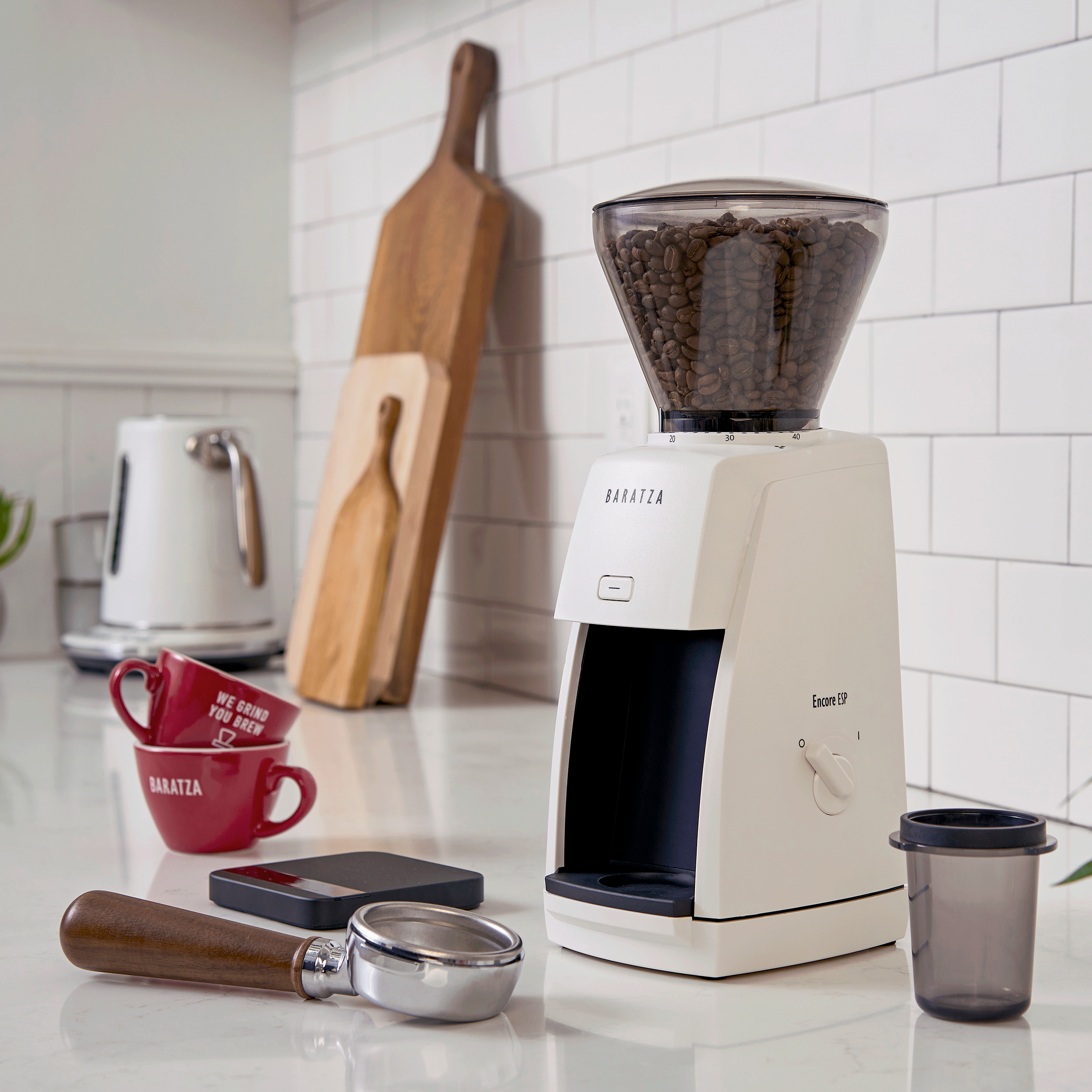 Baratza Encore ESP coffee grinder with coffee beans, portafilter, dosing cup, and espresso cups on a kitchen counter.