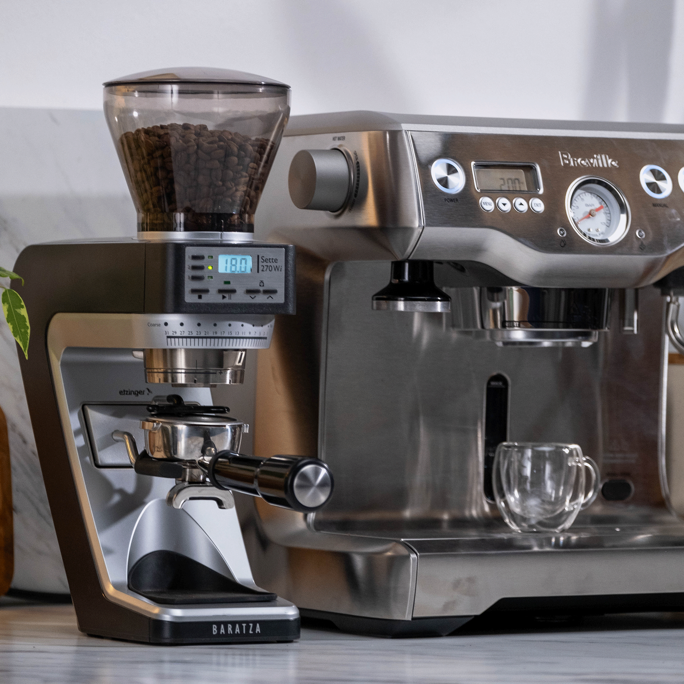 Baratza Sette 270Wi coffee grinder with portafilter beside a Breville espresso machine and glass espresso cup.