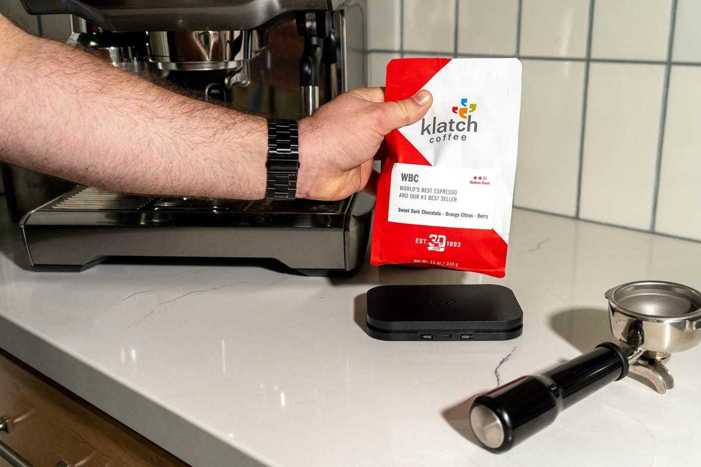 A hand placing a 310g of WBC espresso onto a Bottomless Smart scale that is placed on kitchen counter.