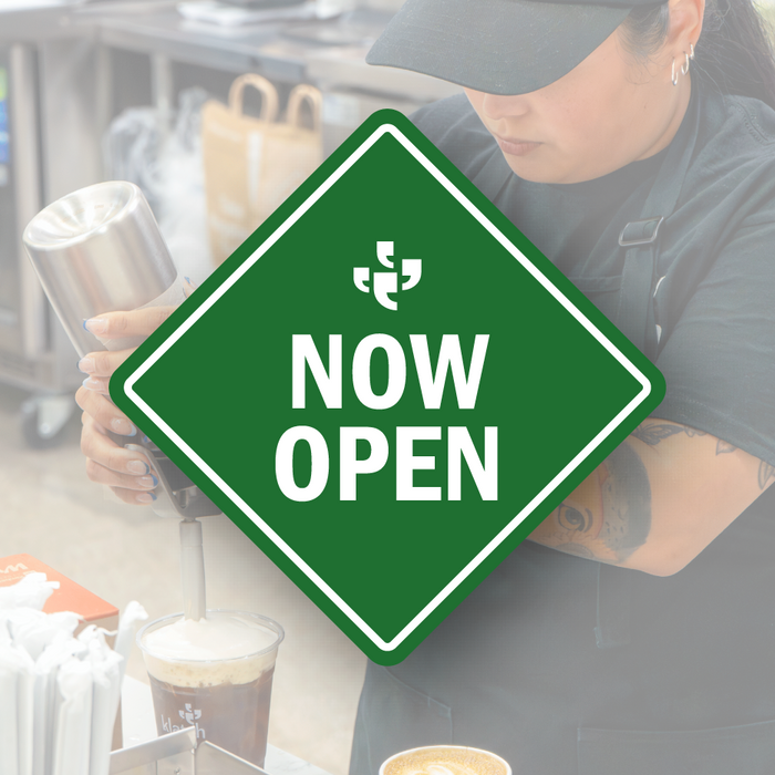 A green diamond-shaped vector sign with the Klatch Coffee logo at the top and “Now Open” beneath it, placed over a photo of a Klatch Coffee barista.  