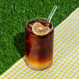 Glass of Klatch Coffee's Cold Brew Lemonade on a grassy background, garnished with a dried lemon wedge.