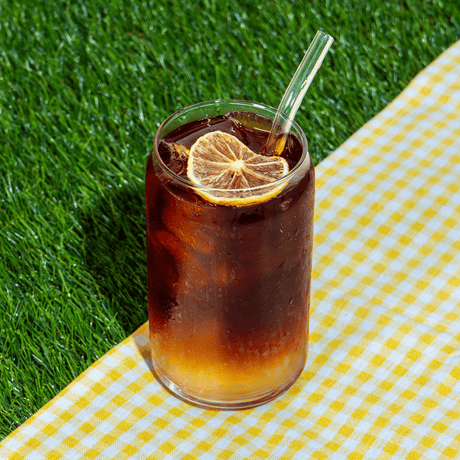 Glass of Klatch Coffee's Cold Brew Lemonade on a grassy background, garnished with a dried lemon wedge.