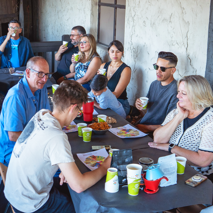 Group of people sitting around a table with drinks and food, in an indoor setting.