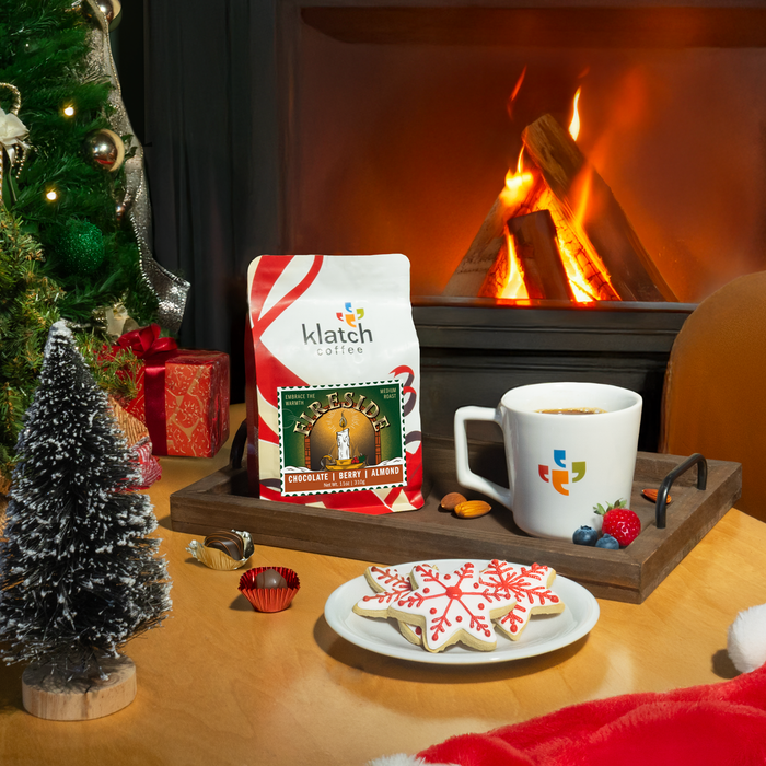 Klatch Fireside coffee bag on a table with cookies and chocolate, set in front of a fireplace and Christmas tree.