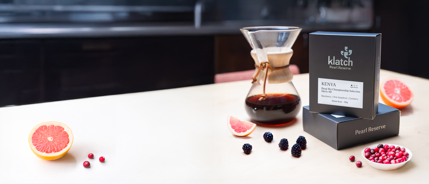 Chemex coffee maker with Klatch coffee Pearl Kenya Berg Wu package on a table with fruits and berries.