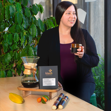 Woman holding a mug with a coffee setup including a Chemex and a Pearl Reserve Coffee on the table.