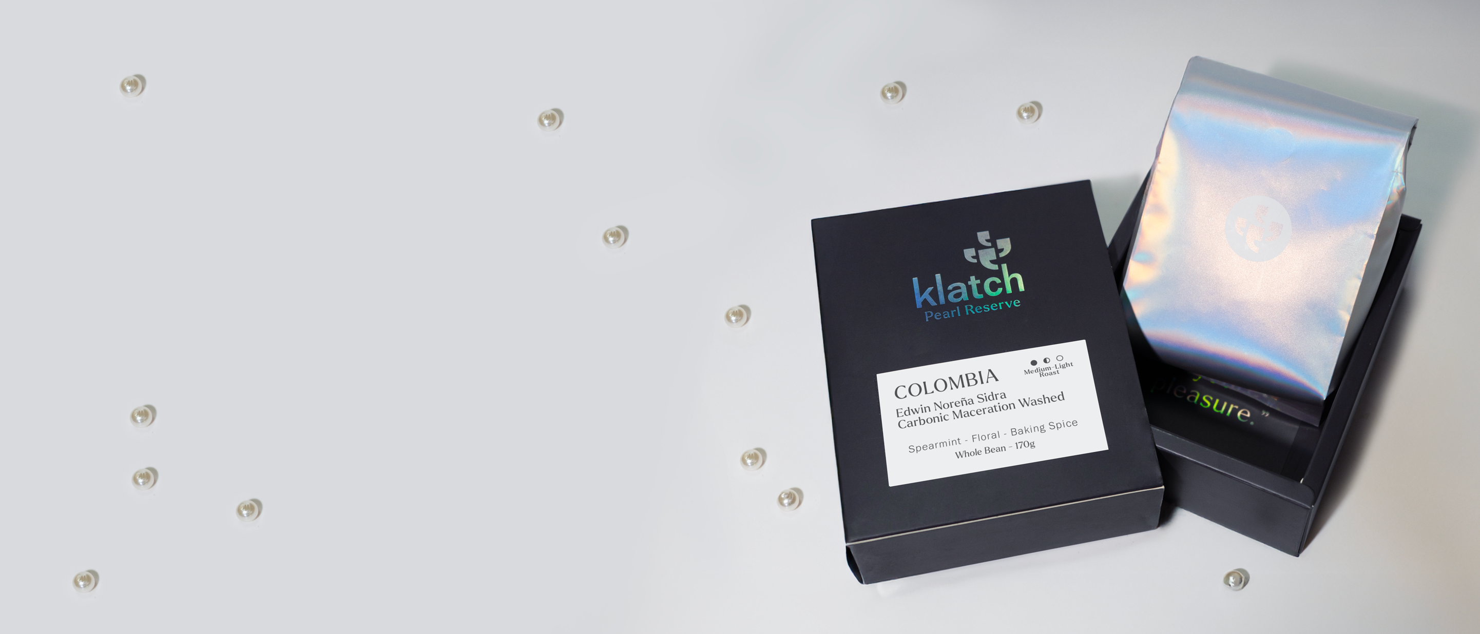 Klatch Pearl Reserve coffee packaging with a black box and colorful bag on a light gray background. 