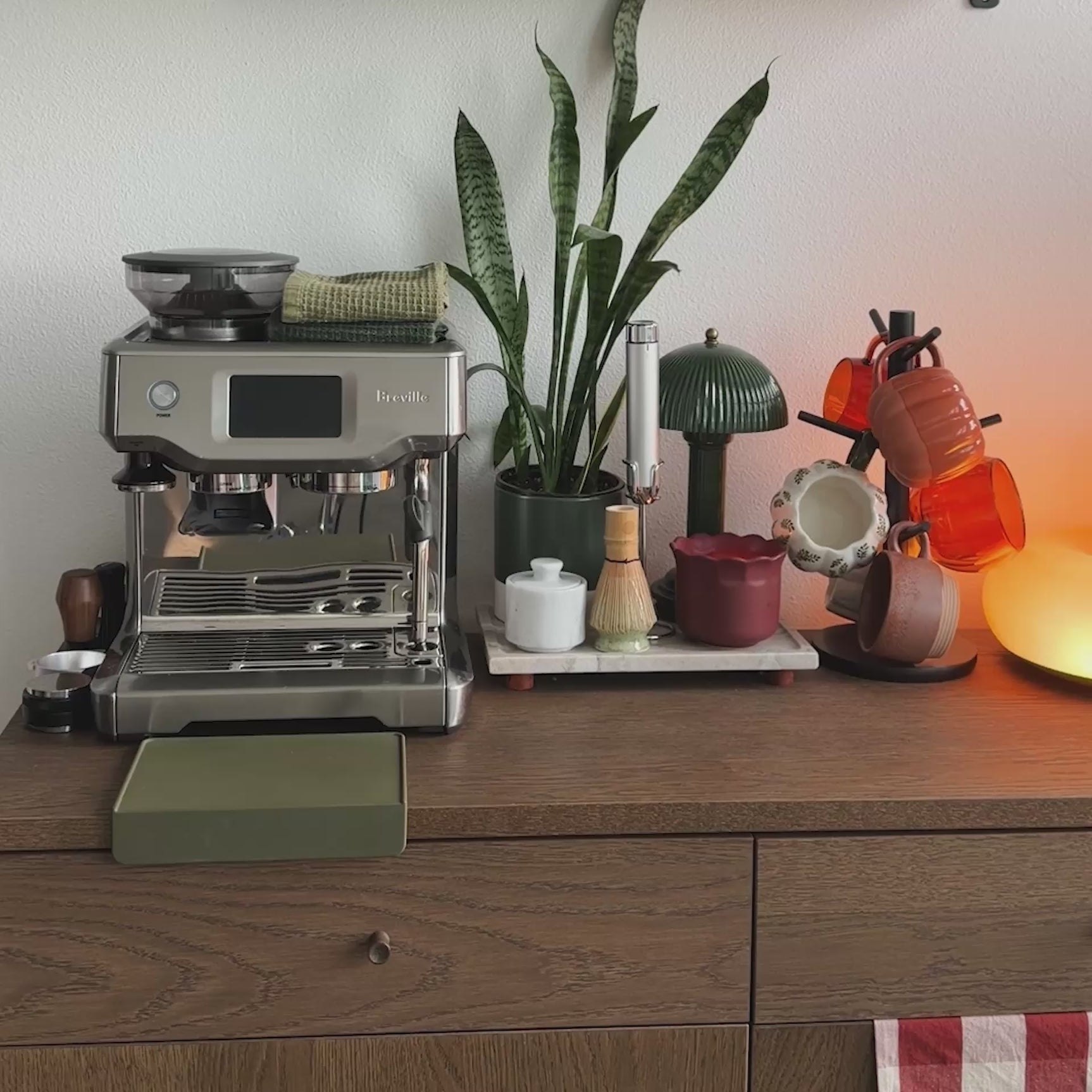 A woman uses a Breville espresso machine to grind coffee, pull a shot of espresso, and steam milk to make a latte.