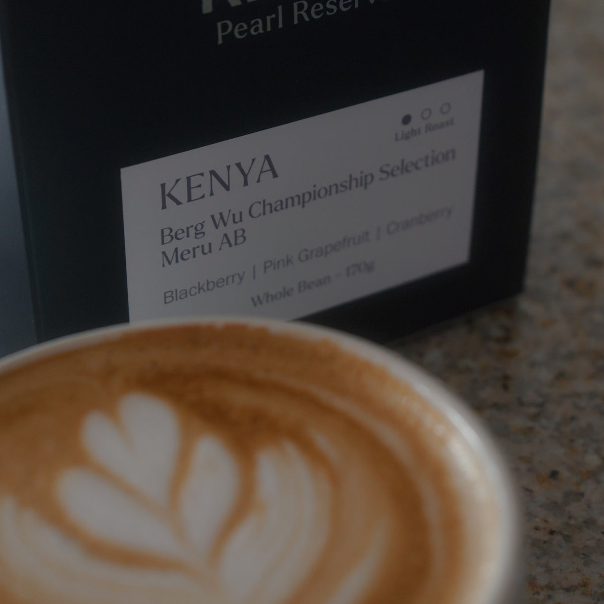 A barista prepares Klatch Coffee’s Kenya Berg Wu Championship Selection as espresso. The beans are ground, tamped, and then brewed in an espresso machine. The espresso is then used to create a latte in a ceramic mug.