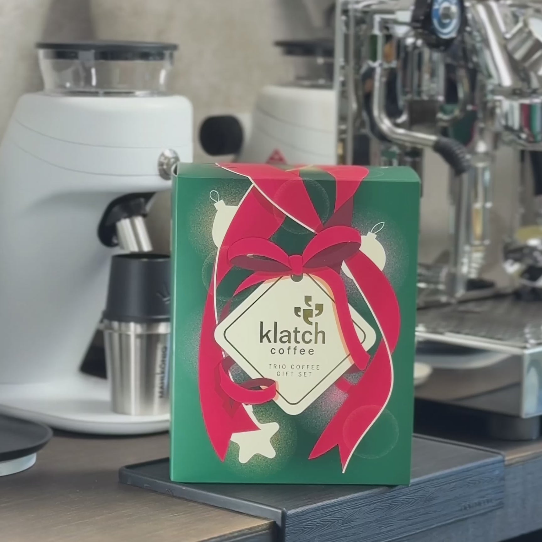 A person opens a Klatch Coffee Espresso Trio box, grinds coffee beans, and brews a shot of espresso using an espresso machine. The espresso is poured into a green glass.