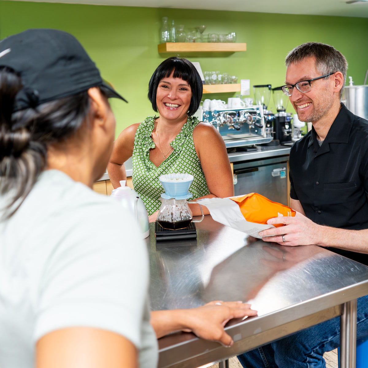 Three people smiling and enjoying a pour over coffee.