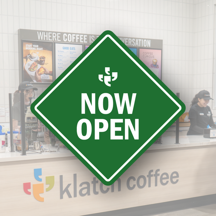 A green diamond-shaped vector sign with the Klatch Coffee logo at the top and “Now Open” beneath it, placed over a photo of a Klatch Coffee cafe. 